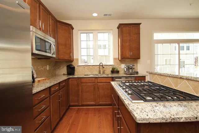 a kitchen with kitchen island granite countertop stainless steel appliances a sink a stove a microwave a refrigerator and cabinets