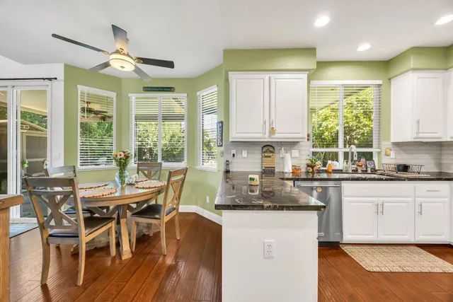 a kitchen with stainless steel appliances granite countertop a stove a sink a refrigerator and white cabinets with wooden floor