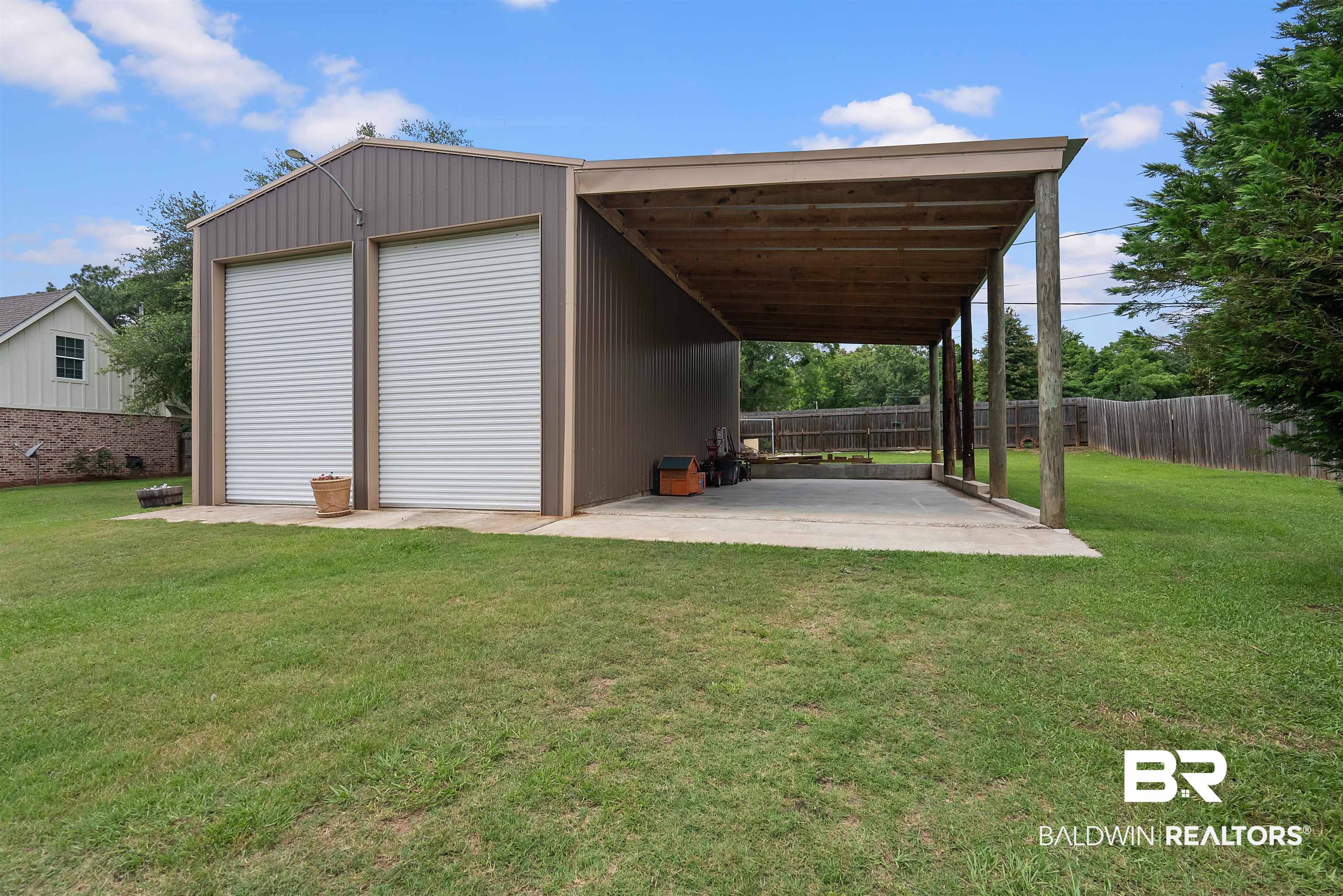 12070 Comalander Road Fairhope, AL 36532 - Photo 2 of 50 Metal outbuilding featuring two roll-up doors, a covered concrete patio, and a privacy fence