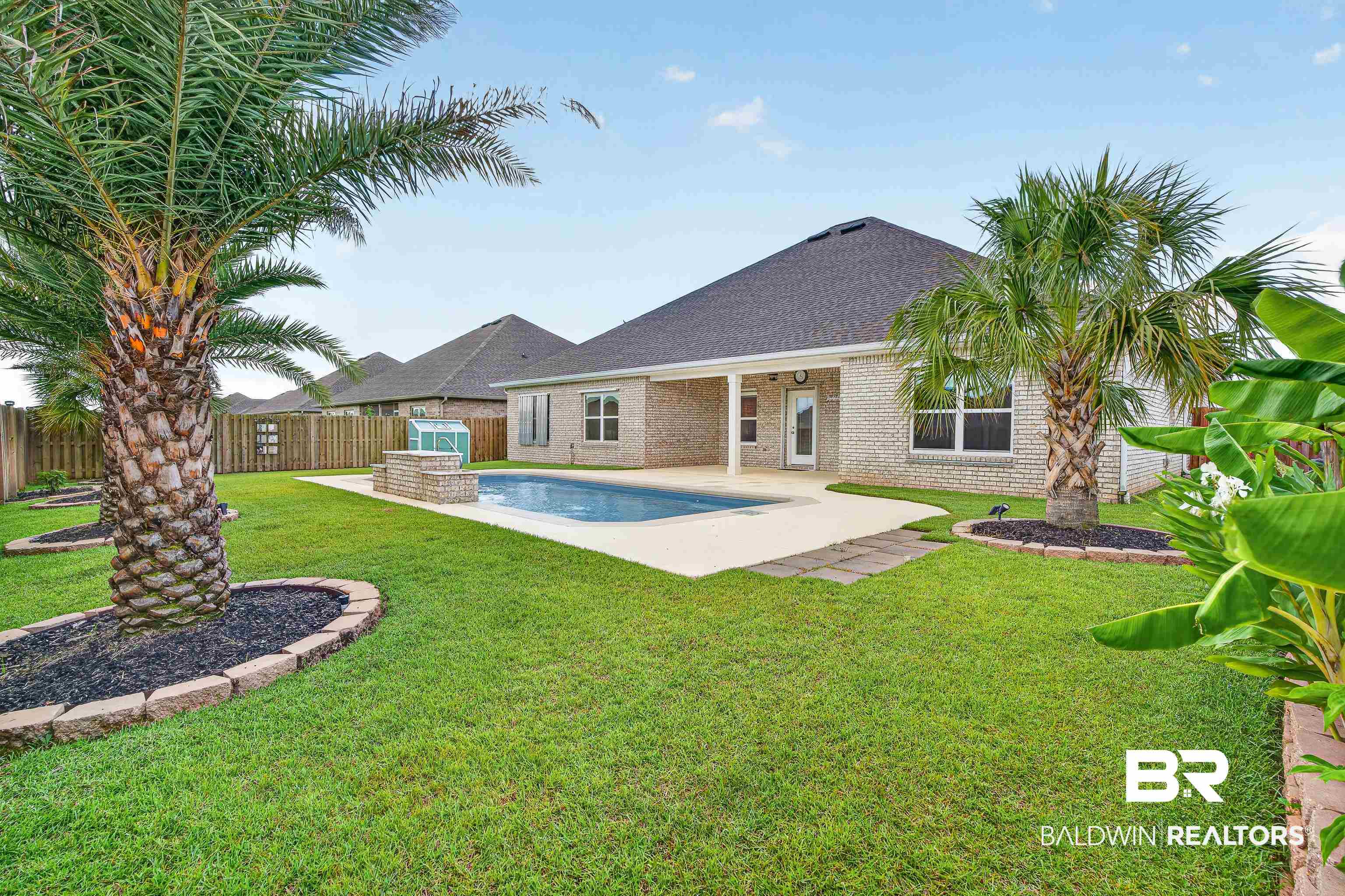1724 Partridge Street Foley, AL 36535 - Photo 50 of 62 Expansive backyard featuring a rectangular in-ground pool with a surrounding concrete patio, a covered patio area, a raised planter with a stone-finish border, and mature palm trees