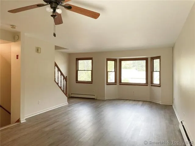 an empty room with wooden floor fan and windows