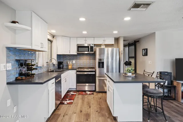 a kitchen with stainless steel appliances granite countertop a refrigerator a stove a sink a dining table and chairs with wooden floor