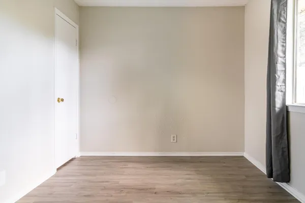 a view of an empty room with wooden floor and a window