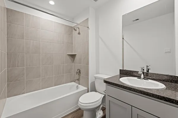 a bathroom with a granite countertop sink a toilet a mirror a bathtub and shower