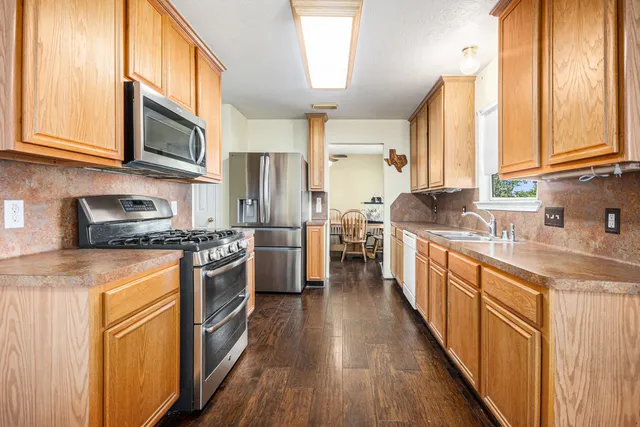 a kitchen with stainless steel appliances granite countertop a stove a sink dishwasher a refrigerator and a microwave oven with wooden floor