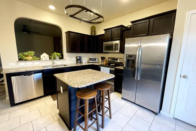 a kitchen with stainless steel appliances kitchen island granite countertop a table a refrigerator and a microwave