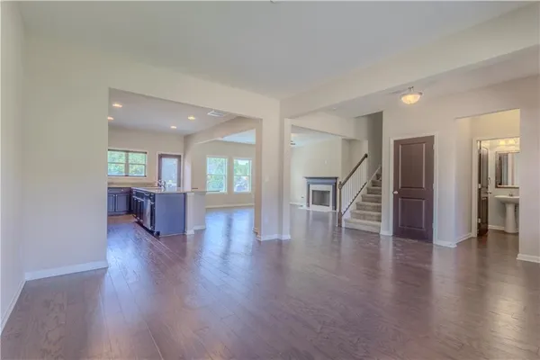 a view of an empty room with wooden floor and a kitchen