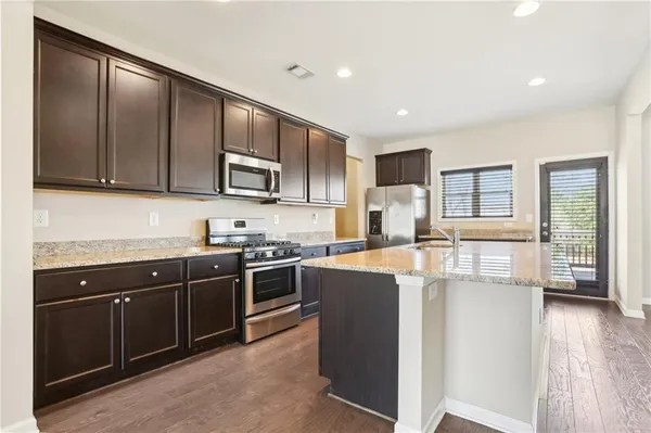 a kitchen with stainless steel appliances granite countertop wooden cabinets a refrigerator a stove a sink and dishwasher with wooden floor