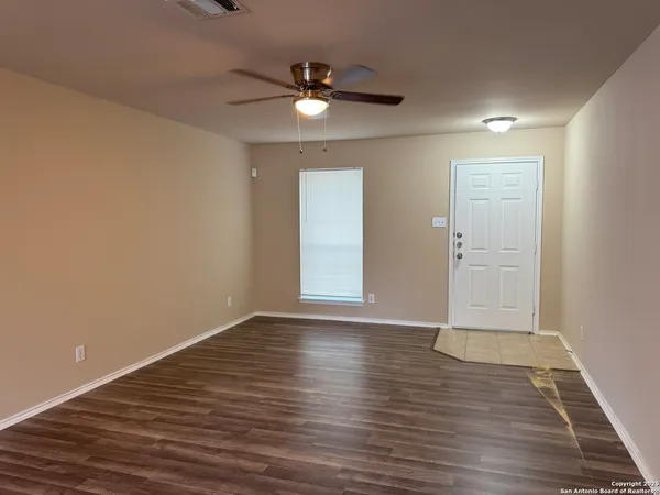 a view of an empty room with wooden floor and a ceiling fan