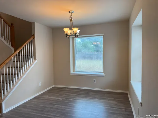 an empty room with wooden floor chandelier and windows