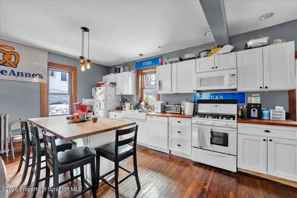a kitchen with a stove a sink dishwasher white refrigerator a dining table and chairs with wooden floor