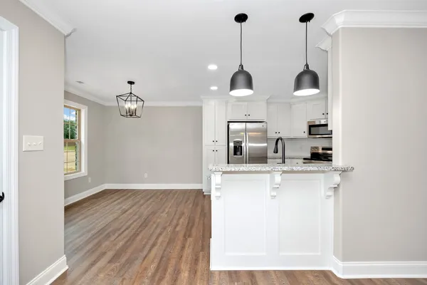a view of a kitchen with stainless steel appliances granite countertop a sink a refrigerator and a wooden floor