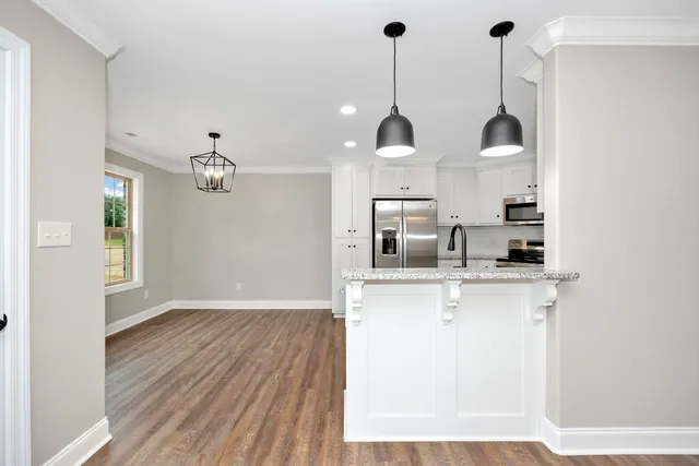 a view of a kitchen with stainless steel appliances granite countertop a sink a refrigerator and a wooden floor