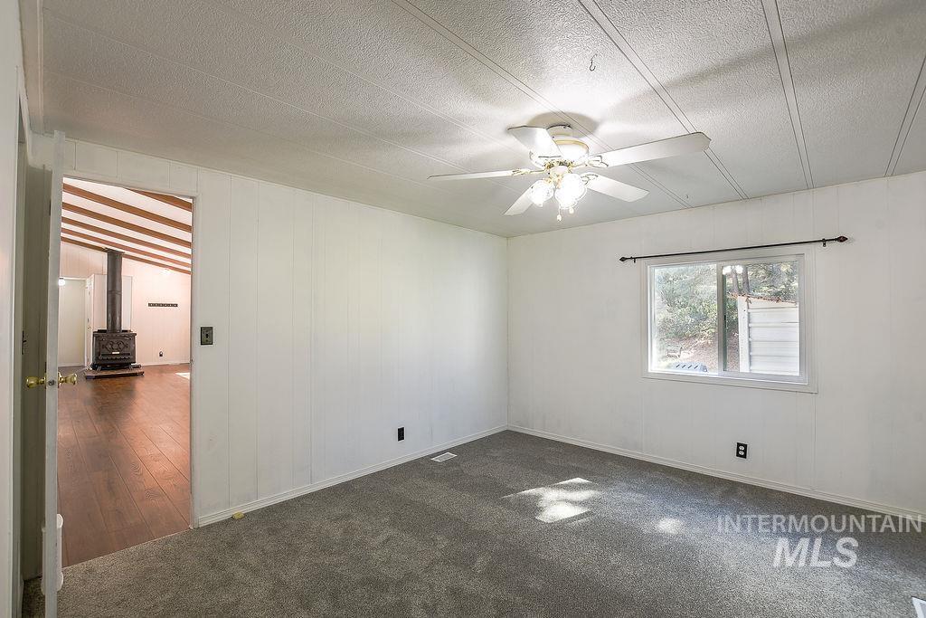609 North Almon Street, Unit 2011 Moscow, ID 83843 - Photo 33 of 45 Unfurnished room with ceiling fan, a wood stove, wood walls, dark colored carpet, and a textured ceiling