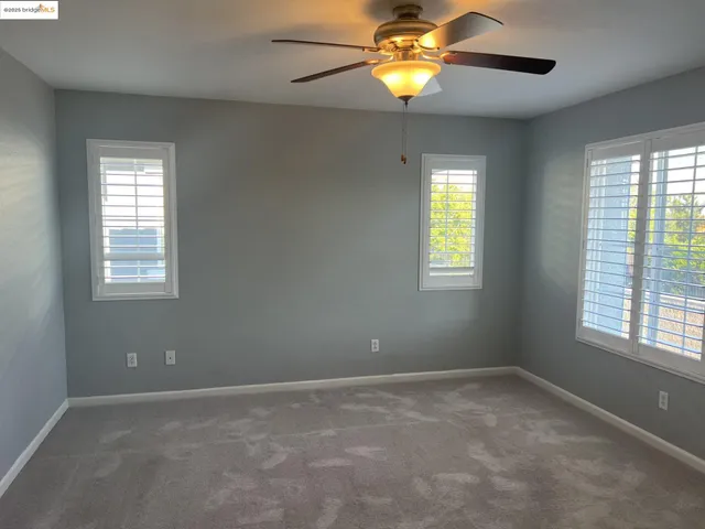 an empty room with windows and chandelier fan