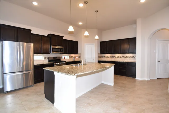 a kitchen with stainless steel appliances kitchen island granite countertop a refrigerator a stove a sink and a microwave with wooden floor