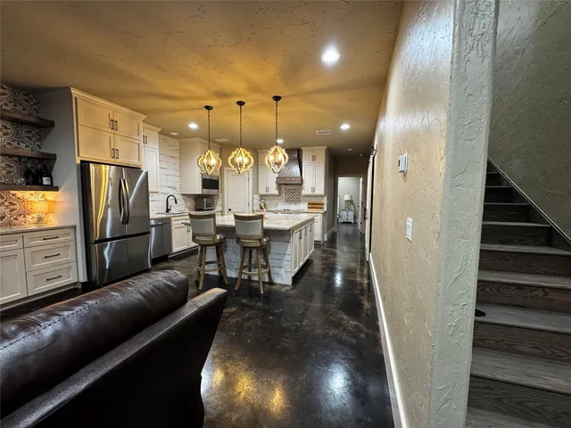 a living room with stainless steel appliances furniture a rug and a view of kitchen