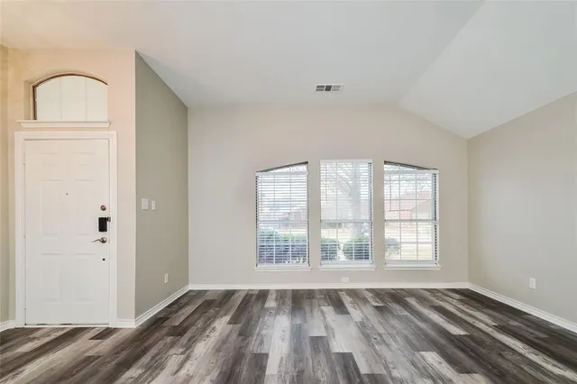 an empty room with wooden floor cabinet and windows