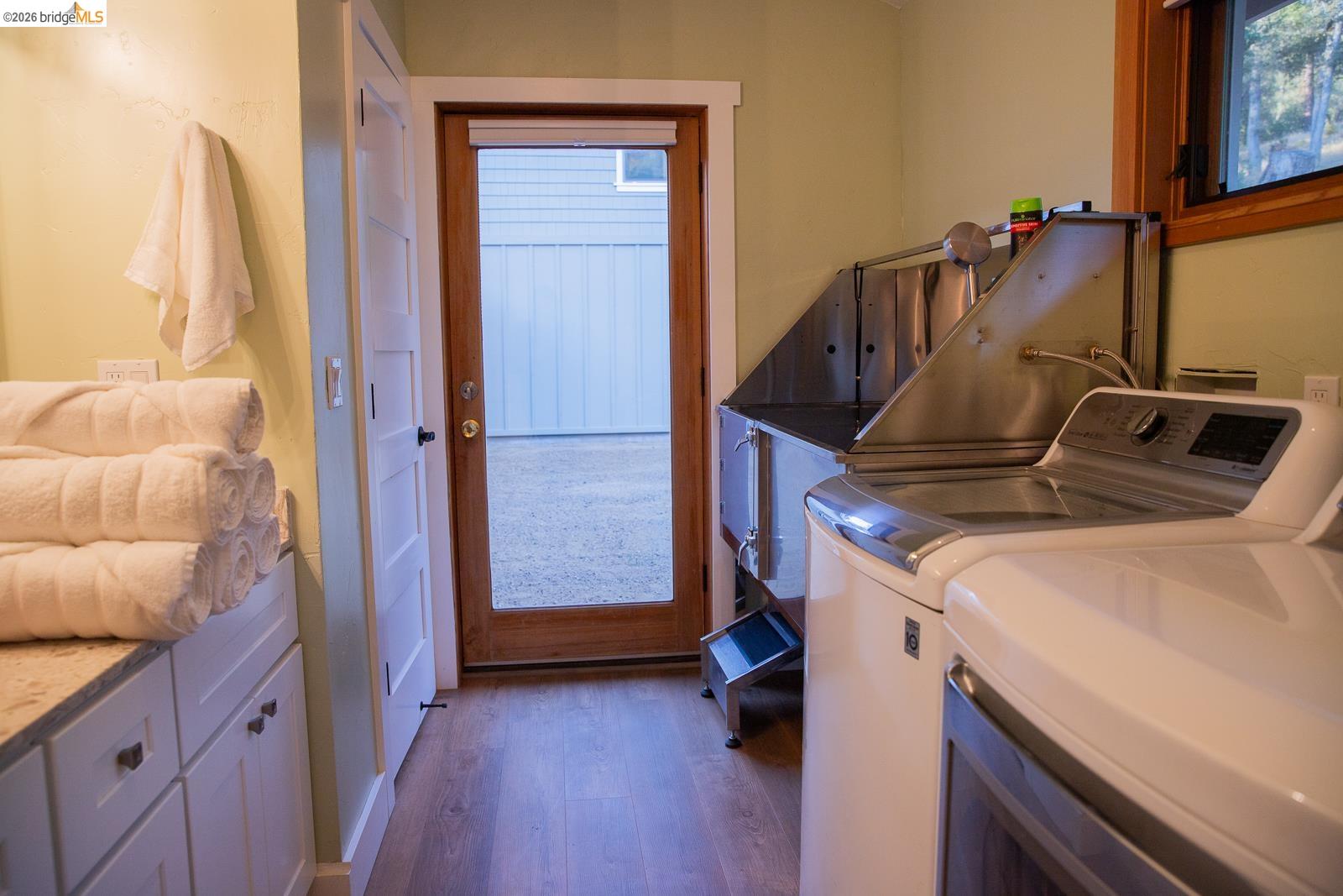 18399 Lime Kiln Road Sonora, CA 95370 - Photo 13 of 36 Functional utility room featuring a full-light wood-frame door, wood-finish flooring, built-in cabinetry with stone countertop, stainless steel utility sink, and side-by-side laundry appliances