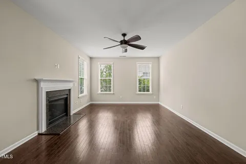 an empty room with wooden floor fireplace and windows