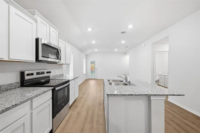 a kitchen with granite countertop stainless steel appliances a sink a stove top oven a counter space and cabinets