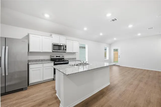 a kitchen with stainless steel appliances granite countertop a stove top oven a sink dishwasher a refrigerator and white cabinets with wooden floor