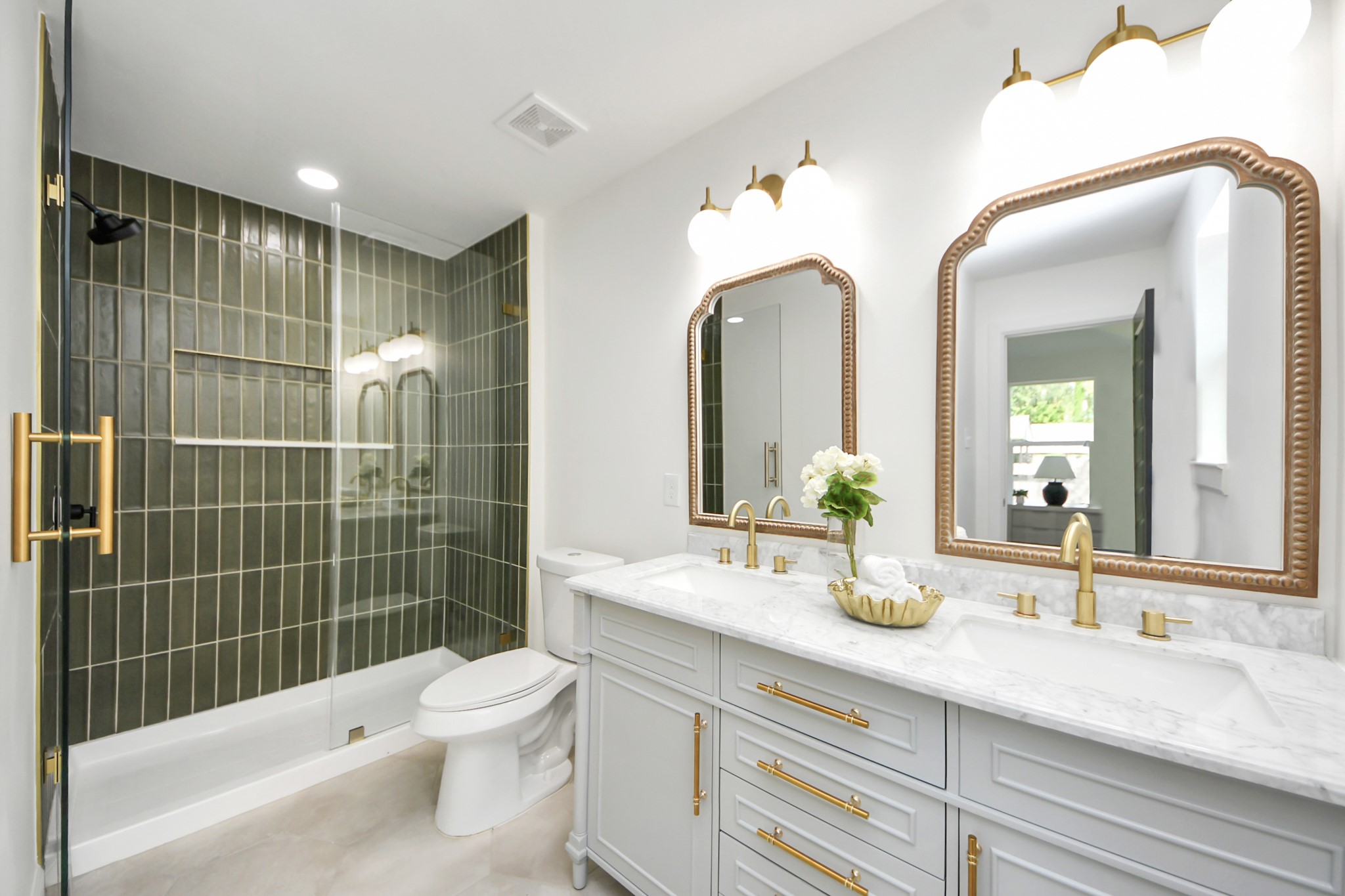 1737 Tabor Street Houston, TX 77009 - Photo 1 of 46 This bathroom features a sleek design with a modern glass-enclosed shower and stylish green tile. It includes a double vanity with elegant gold fixtures and large mirrors, providing a luxurious and functional space.