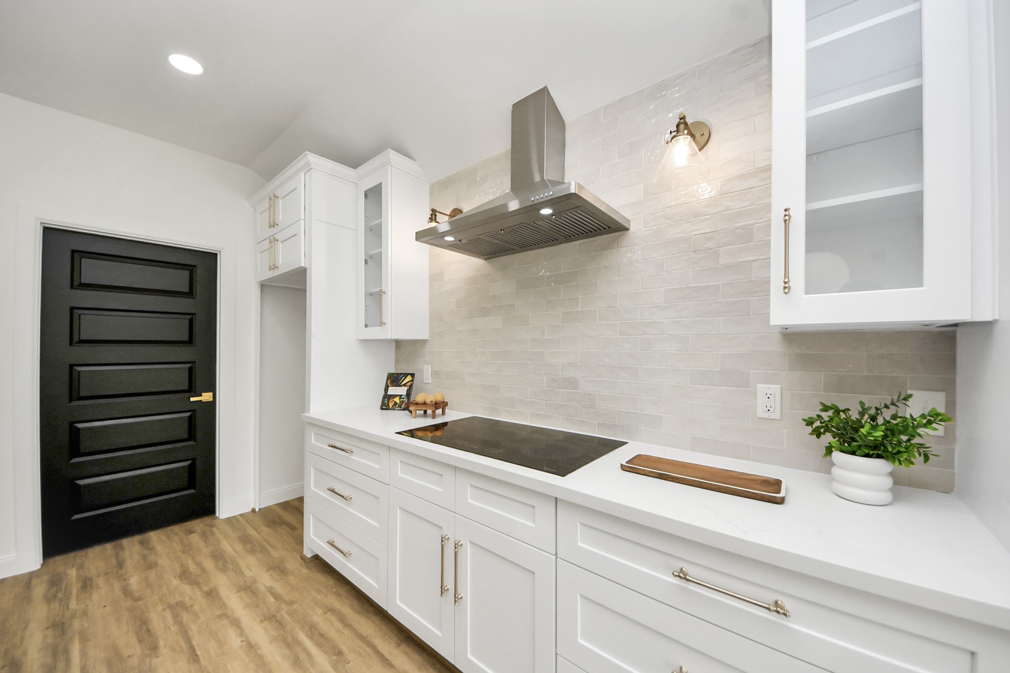 1737 Tabor Street Houston, TX 77009 - Photo 16 of 46 A beautifully curated kitchen where modern white cabinetry with glass accents meets warm brass hardware and soft, ambient lighting. The sleek induction cooktop and stainless steel range hood offer a streamlined look, while a beige subway tile backsplash brings just the right touch of warmth and texture.