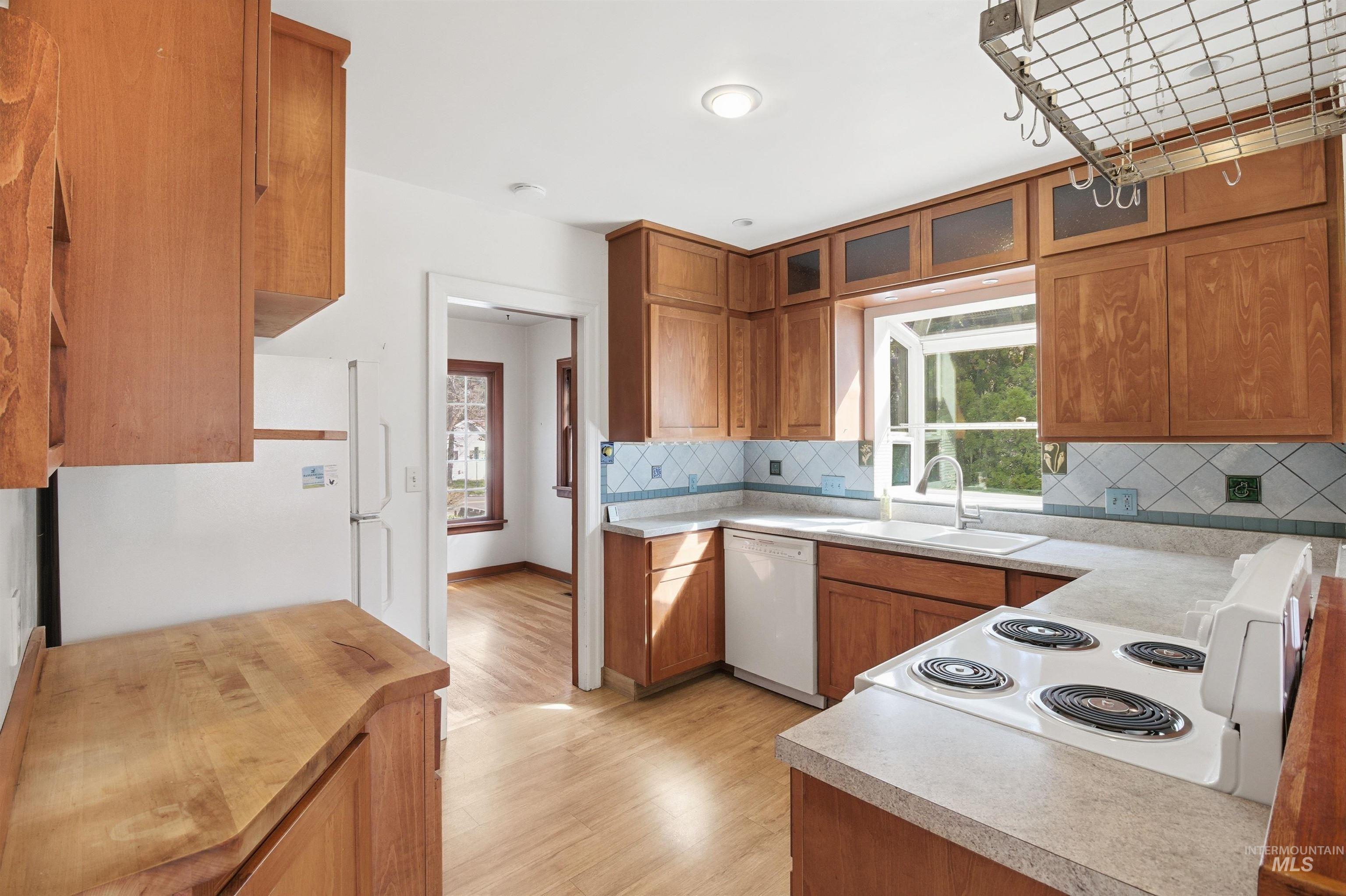 1117 East 6th Street Moscow, ID 83843 - Photo 14 of 46 Kitchen featuring wood finish cabinetry, white appliances, light wood finished floors, glass fronted cabinets, and backsplash