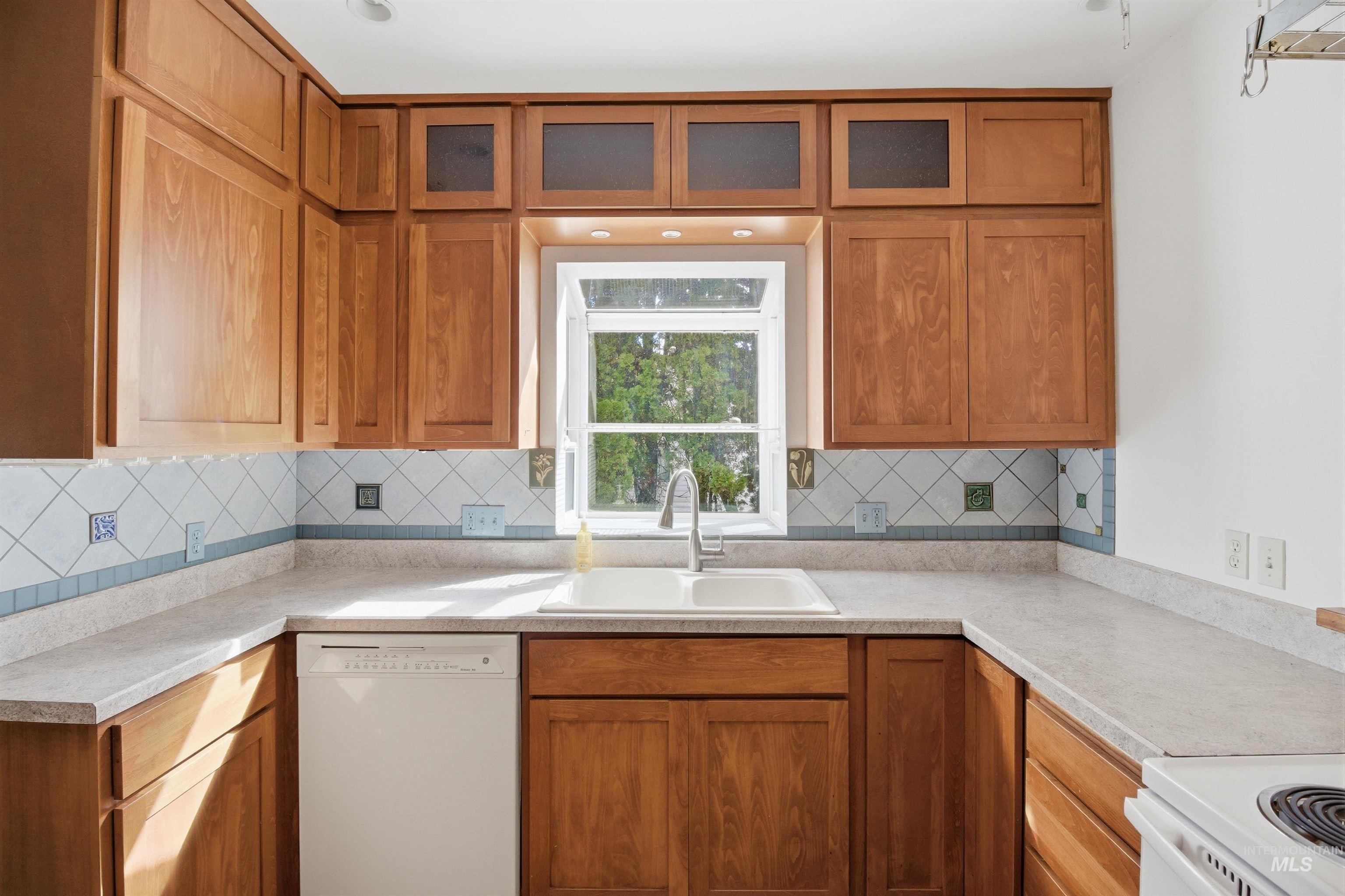 1117 East 6th Street Moscow, ID 83843 - Photo 15 of 46 Kitchen featuring wood finish cabinets, white appliances, glass insert cabinets, light countertops, and tasteful backsplash
