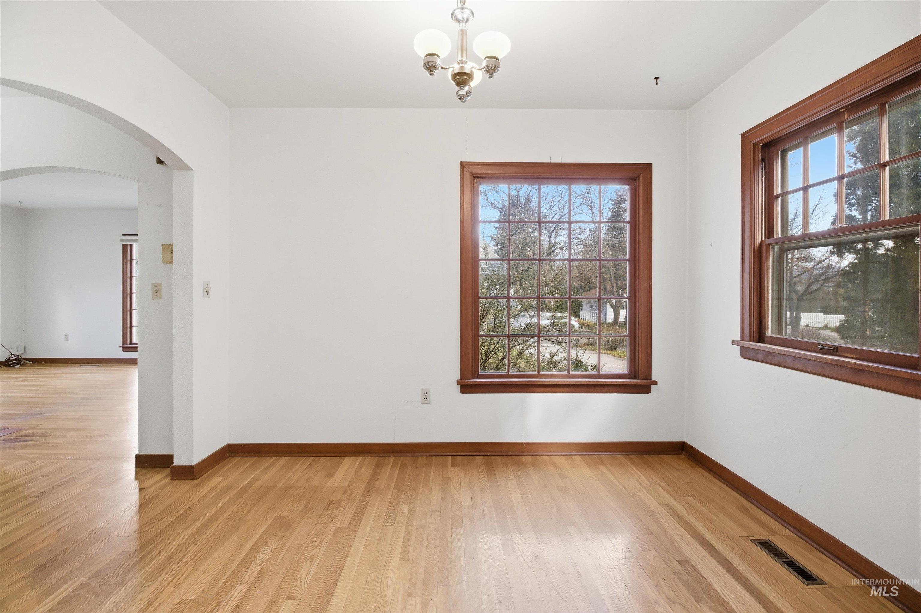 1117 East 6th Street Moscow, ID 83843 - Photo 18 of 46 Empty room featuring arched walkways, light wood finished floors, healthy amount of natural light, and a chandelier