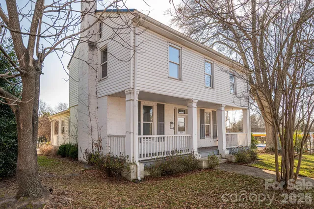 a view of a white house next to a yard with large trees