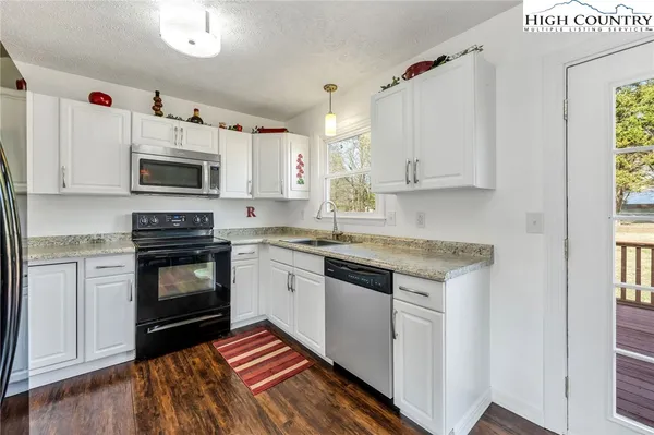 a kitchen with granite countertop a stove top oven a sink dishwasher and a microwave oven on the kitchen countertops with wooden floor