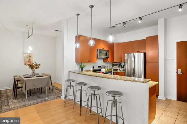 a kitchen with stainless steel appliances granite countertop a refrigerator a sink a dining table and chairs with wooden floor