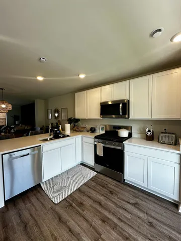 a kitchen with granite countertop a stove top oven a sink dishwasher and white cabinets with wooden floor