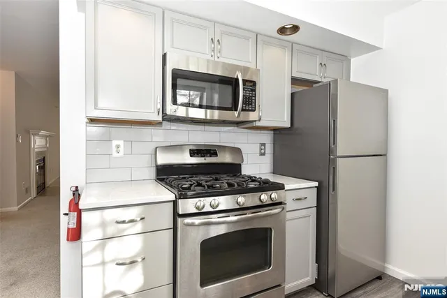 a kitchen with stainless steel appliances granite countertop white cabinets a stove a microwave and a refrigerator