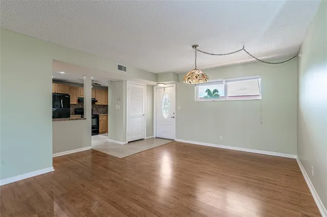 a view of an empty room with wooden floor and kitchen view