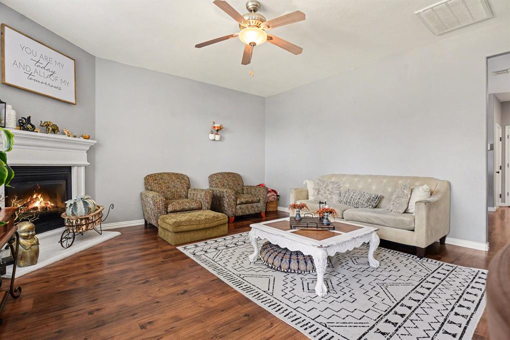 10005 Turrey Rowlett, TX 75089 - Photo 12 of 32 Living area featuring dark wood-style flooring, a lit fireplace, and a ceiling fan