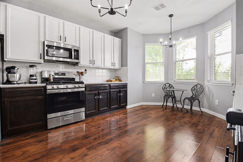10005 Turrey Rowlett, TX 75089 - Photo 8 of 32 Two tone kitchen featuring dual tone cabinets, suspended lighting, stainless steel appliances, light countertops, and dark wood-style flooring