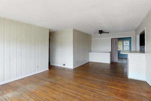 a view of empty room with wooden floor and kitchen view
