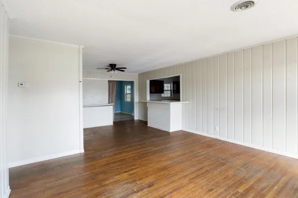 a view of empty room with wooden floor and kitchen