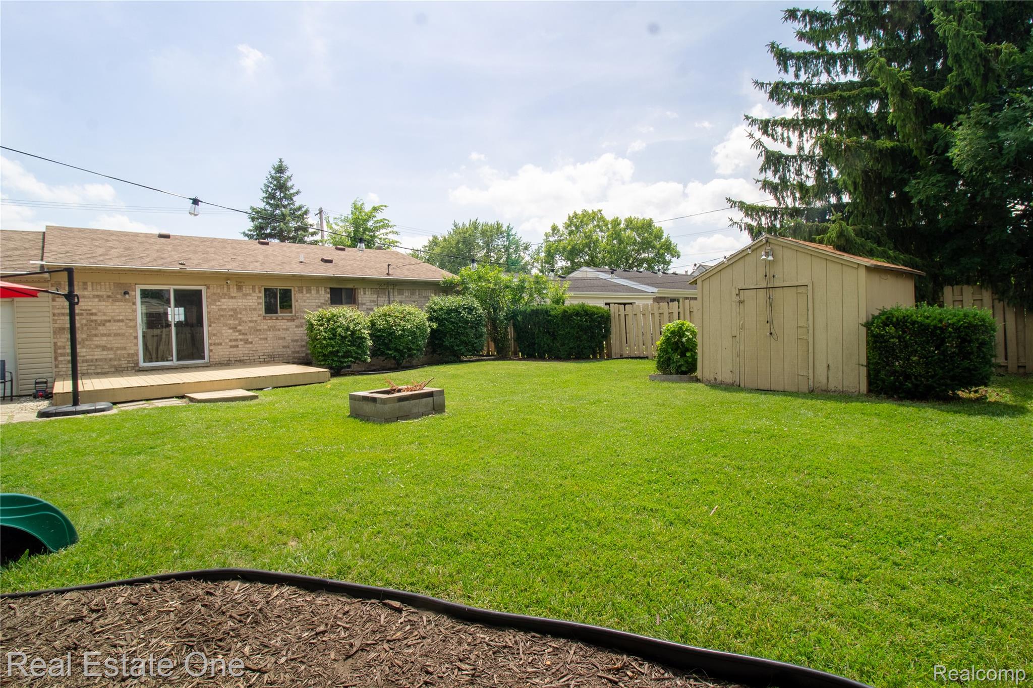 44220 Saltz Road Canton, MI 48187 - Photo 22 of 31 Expansive green lawn with wood privacy fencing, a built-in fire pit, and a wooden storage shed