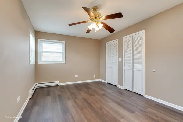 an empty room with wooden floor chandelier fan and windows