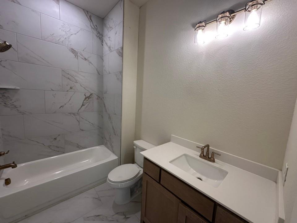 205 Cobb Road Leonard, TX 75452 - Photo 8 of 28 Bathroom featuring a white bathtub, marble-look tile surround and flooring, a toilet, a vanity with a white countertop and integrated sink, and a three-light fixture