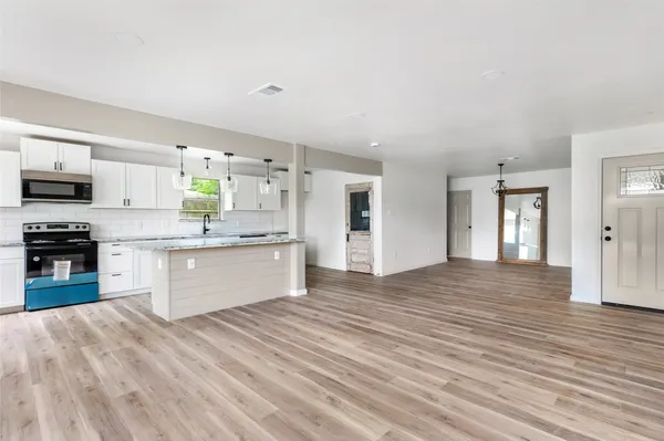 a large kitchen with kitchen island a sink dishwasher stove and white cabinets with wooden floor