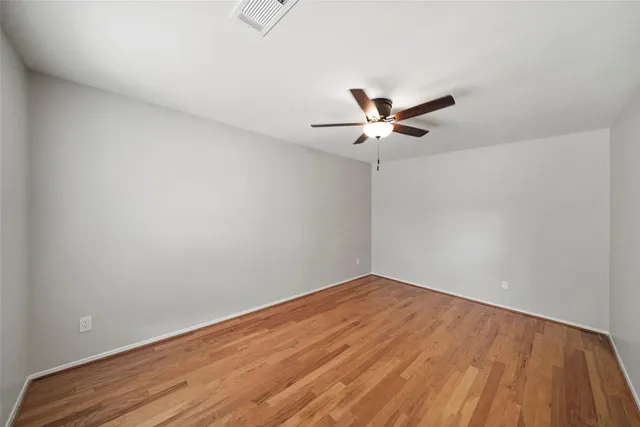 an empty room with wooden floor and ceiling fan