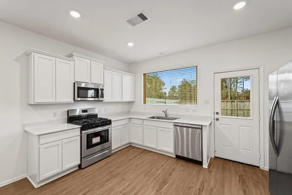 a kitchen with stainless steel appliances granite countertop white cabinets a sink a stove a window and wooden floors