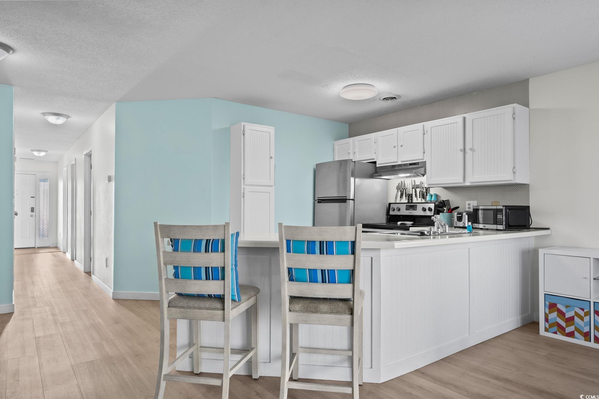 1890 Colony Drive, Unit 16I Myrtle Beach, SC 29575 - Photo 12 of 35 Kitchen with white cabinetry, light wood-type flooring, a kitchen breakfast bar, a peninsula, and a textured ceiling