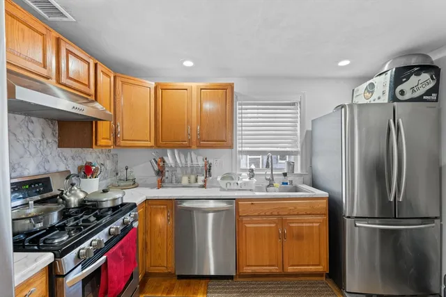 a kitchen with stainless steel appliances a stove a sink a refrigerator cabinets and a window