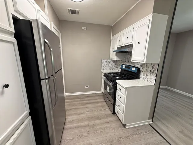 a kitchen with stainless steel appliances a refrigerator a sink and white cabinets